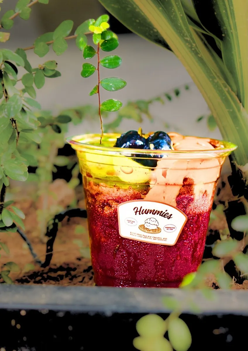 Two acai cups with mango and berry toppings and Hummies stickers against greenery