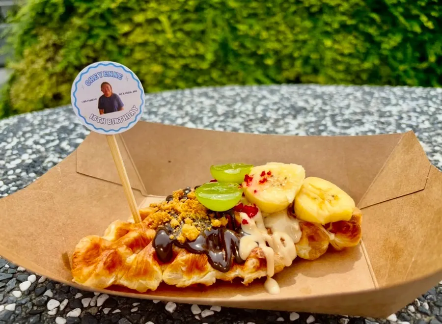 Waffle wand topped with kiwi, banana and berries in a paper tray