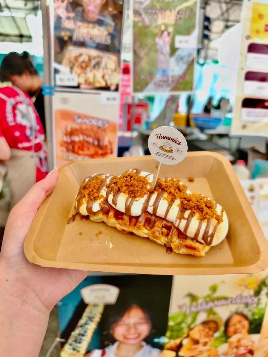 Hand holding a drizzled waffle wand at a fair